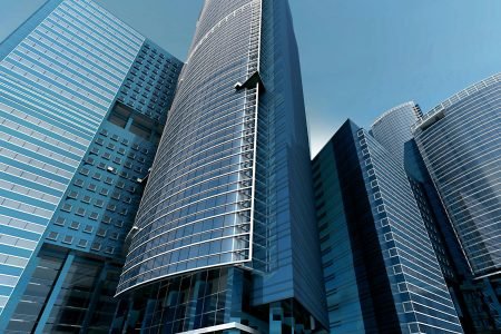 Futuristic urban skyscrapers with glass facades reflecting a vibrant blue sky.