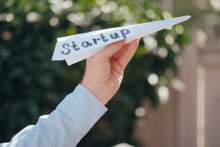 Close-up of a hand holding a paper plane with 'Startup' written, symbolizing a business launch.